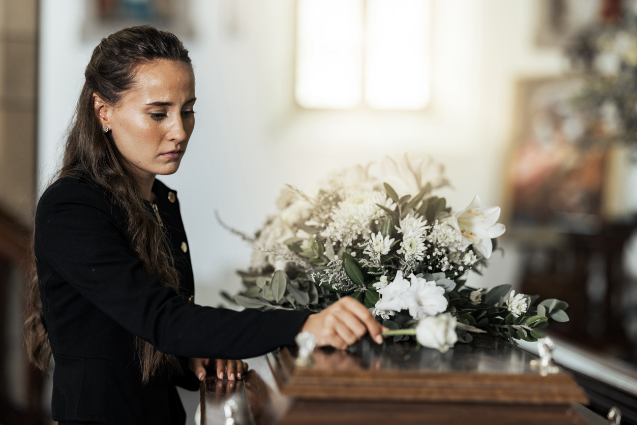 Sad woman placing a white rose on the coffin of a lost loved one.